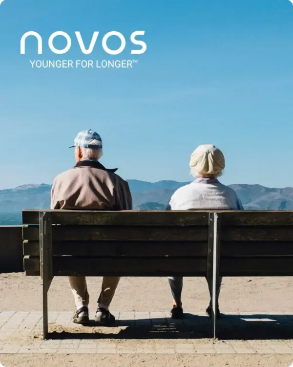 Novos logo over an older couple sitting on a bench by the sea