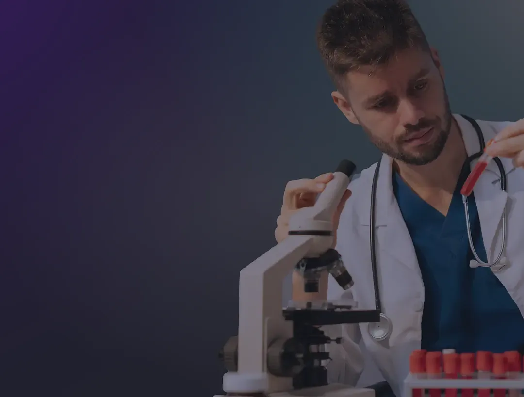Researcher working at a microscope next to blood sample tubes